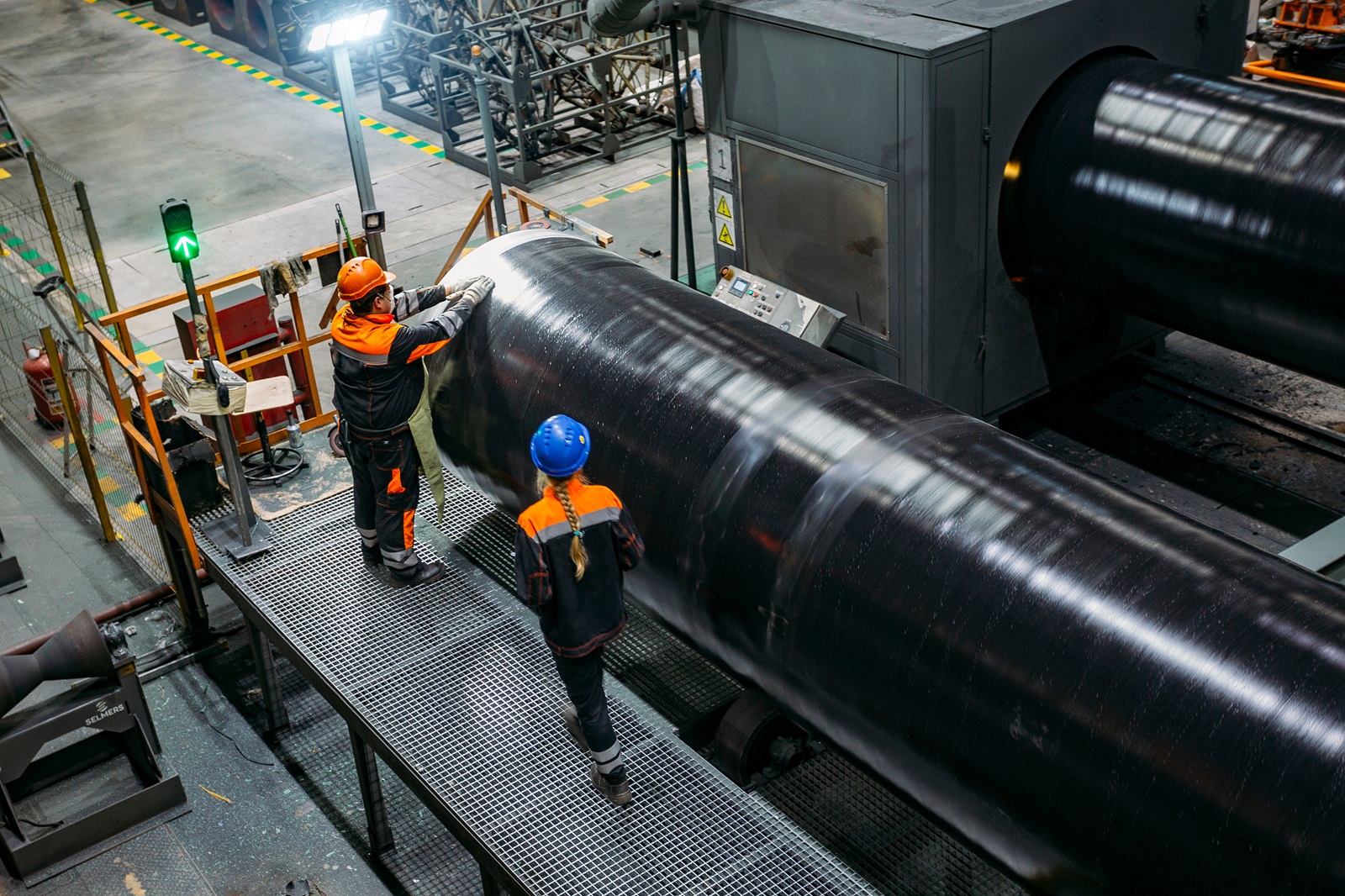 Workers perform pipe coating services in a factory.